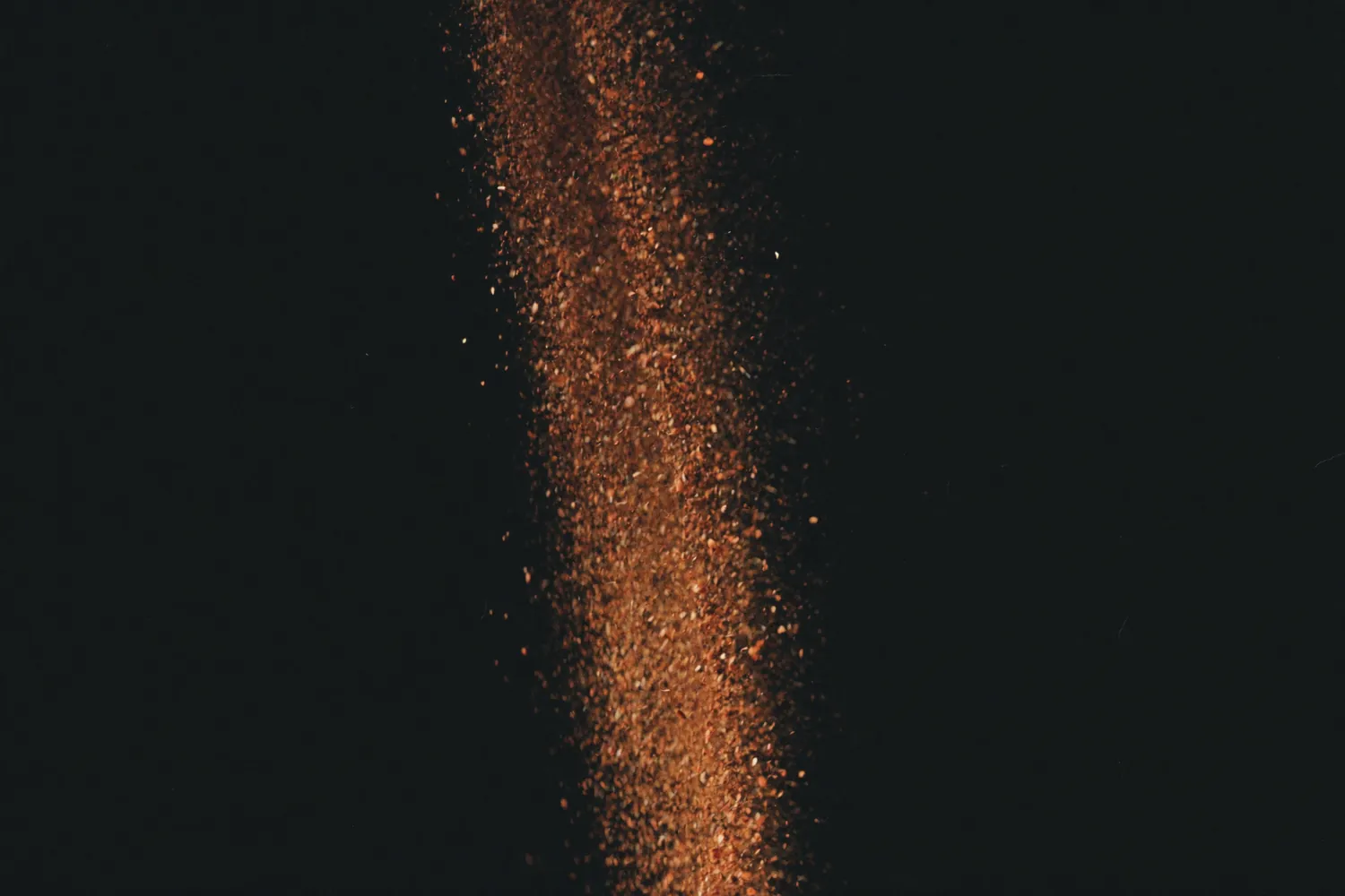 Filete de café moído caindo no ar contra fundo preto, iluminado por trás.